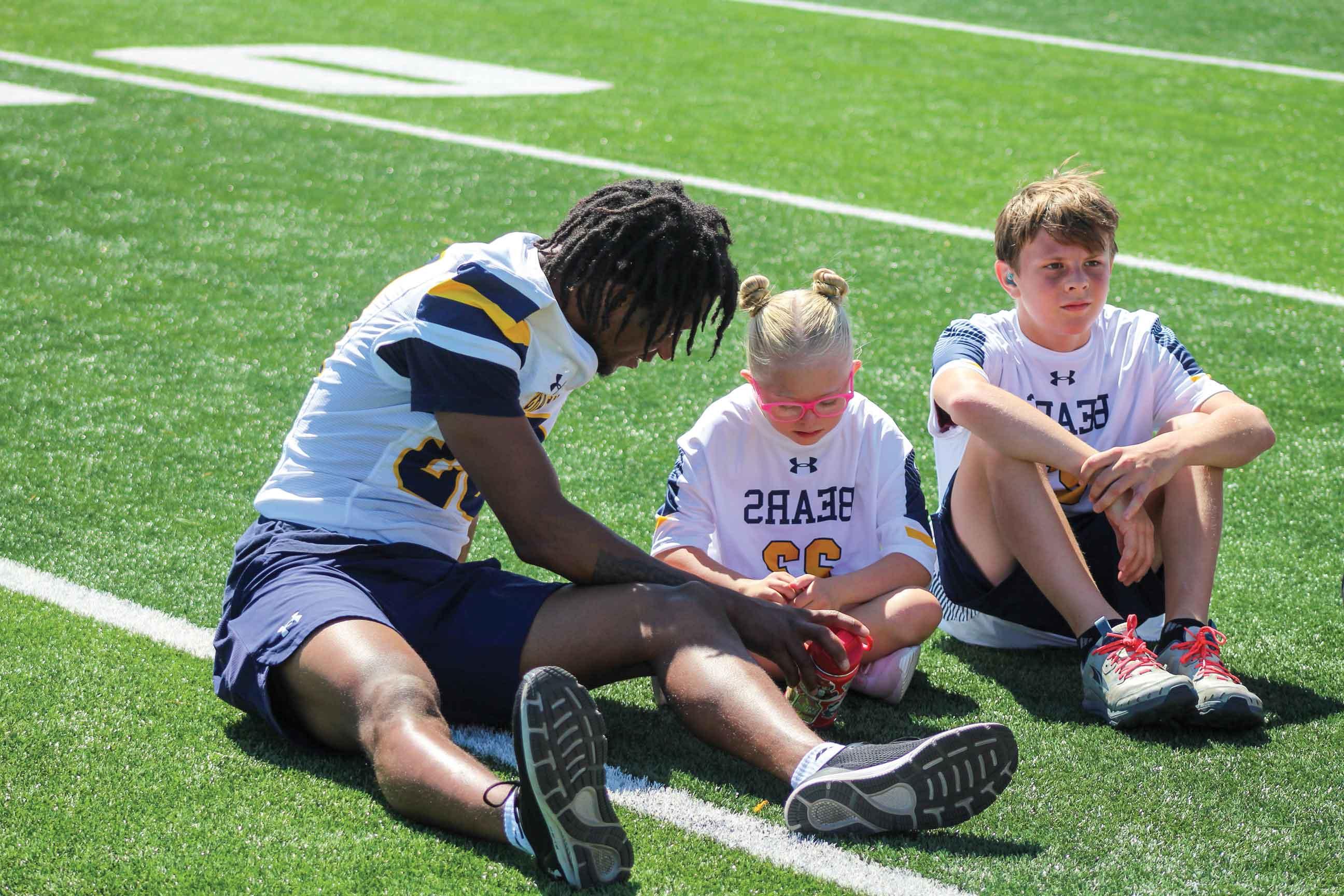 UNC football student-athletes sitting on the field, accompanied by disabled children during the No Limits Camp, f